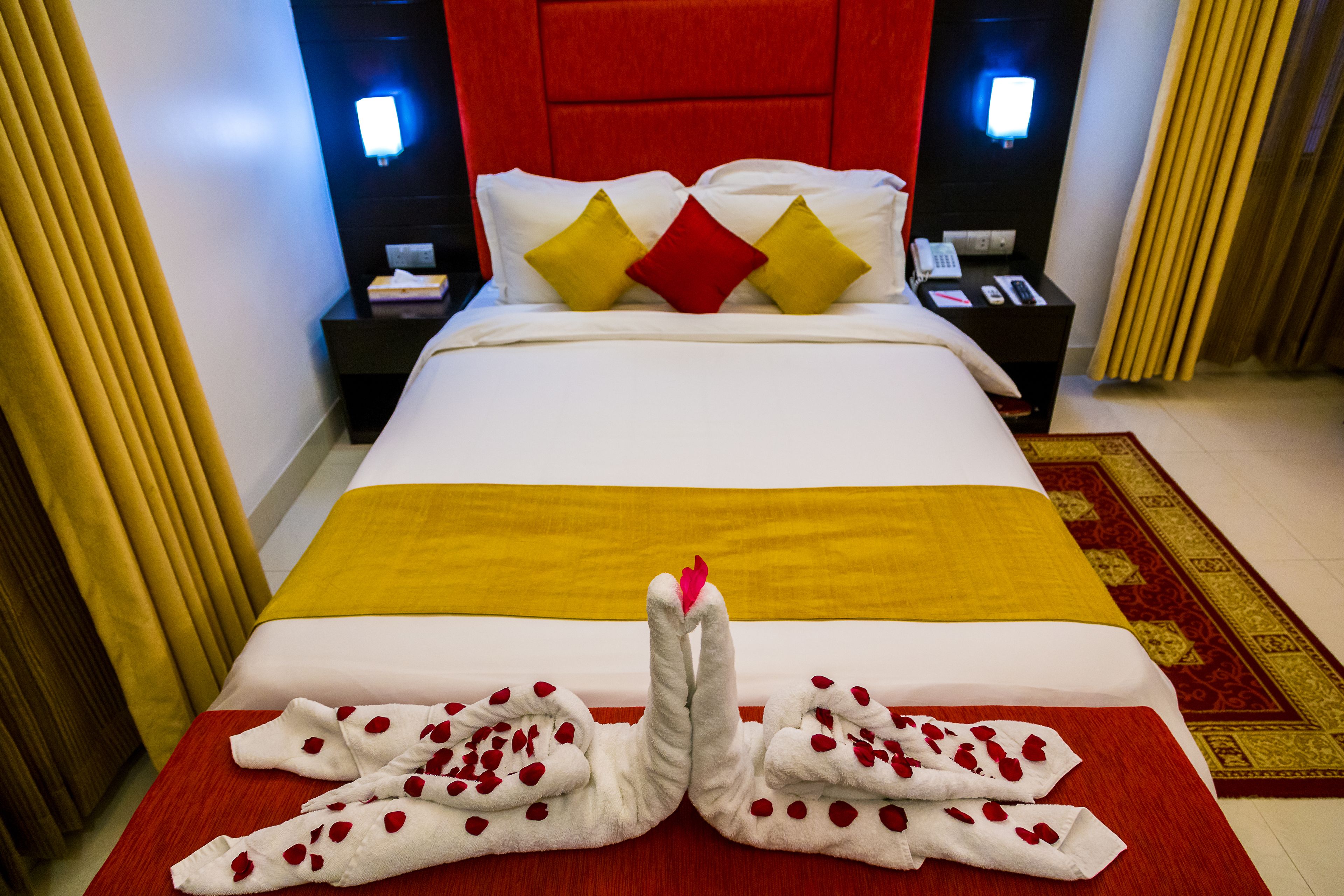 A hotel room with a large bed, a red headboard, and a red and yellow bedspread. There are two nightstands with lamps and a telephone.