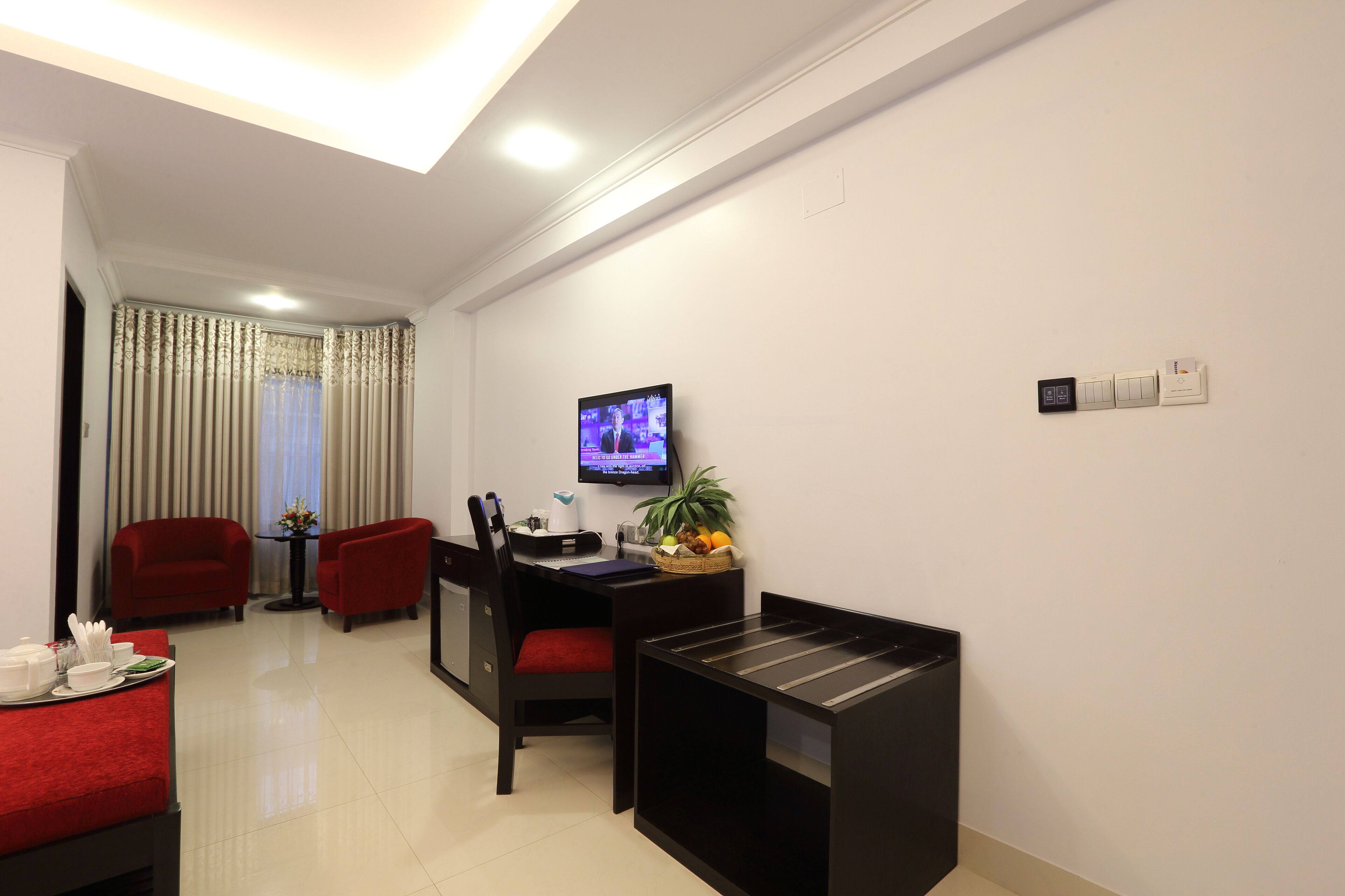 Quarto de hotel com área de refeições, televisão na parede e uma pequena mesa com cesta de frutas.