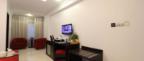 Quarto de hotel com área de refeições, televisão na parede e uma pequena mesa com cesta de frutas.