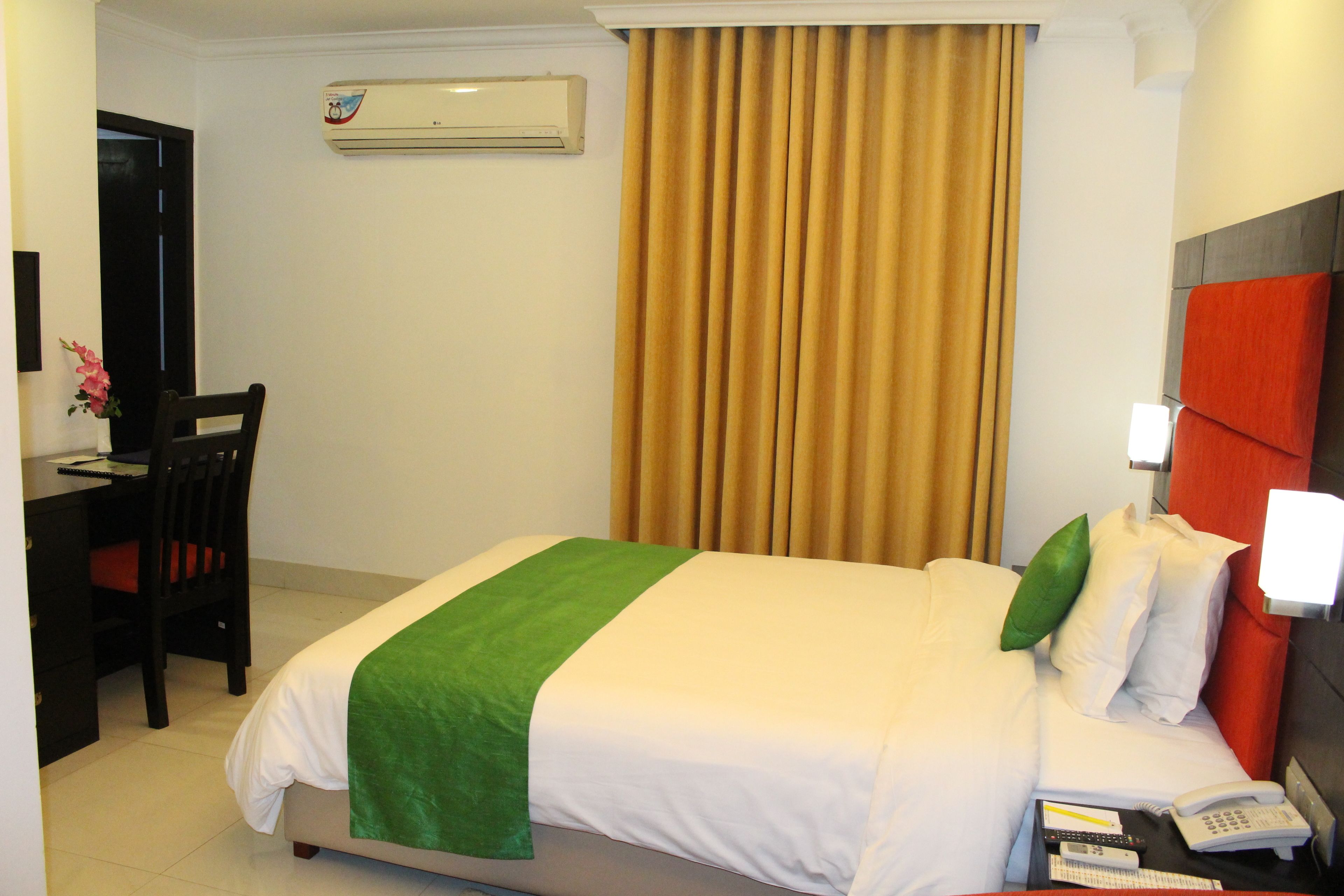 Quarto de hotel com cama, escrivaninha, cadeira, telefone e aparelho de ar condicionado.