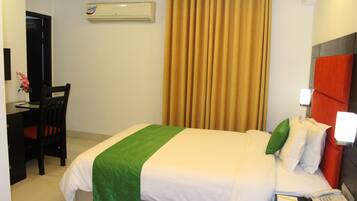 Quarto de hotel com cama, escrivaninha, cadeira, telefone e aparelho de ar condicionado.