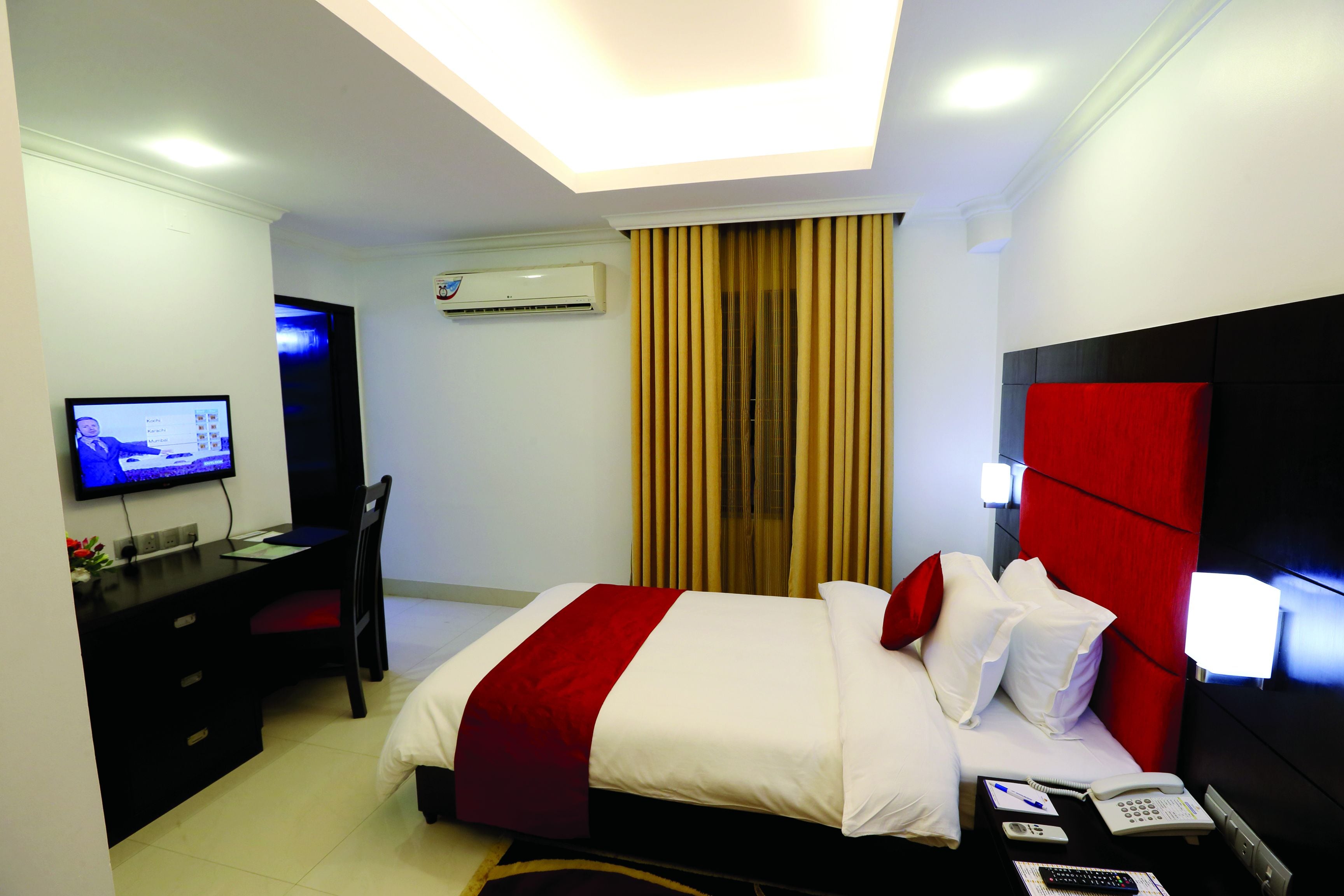 Ein Hotelzimmer mit Bett, Schreibtisch, Stuhl, Fernseher und Klimaanlage.