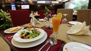 A dining table set with plates, cutlery, a glass of orange juice, and a salad. - Nascent Gardenia Baridhara (Dhaka)