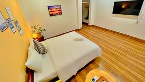 A hotel room with a single bed, a small table with a lamp, a potted plant, and a TV mounted on the wall.