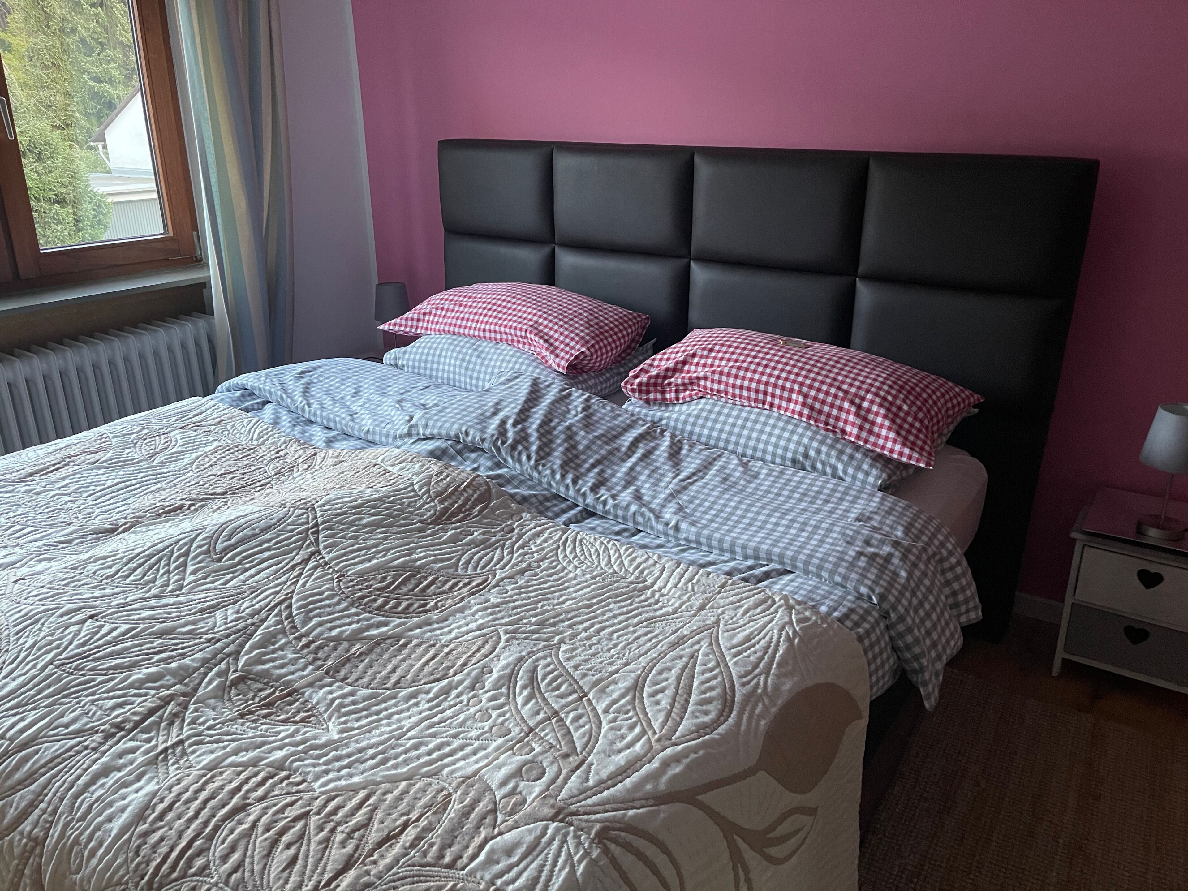Un lit bien fait, avec une literie à motifs, une tête de lit sombre et une table de chevet sur laquelle se trouve une lampe.