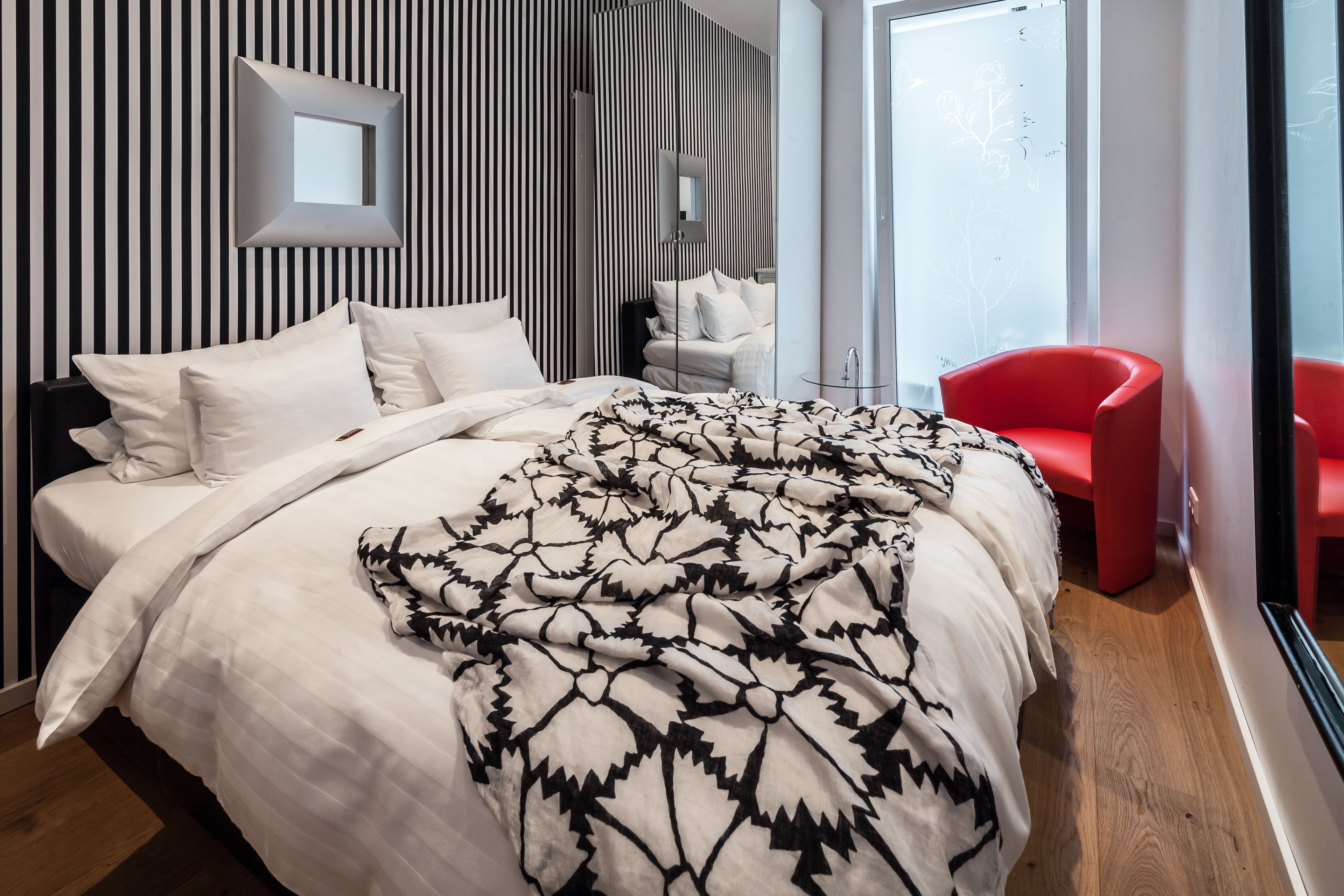 Ein modernes Schlafzimmer mit einem großen Bett, einem roten Sessel und einem Spiegel an der Wand.