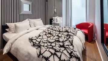 Ein modernes Schlafzimmer mit einem großen Bett, einem roten Sessel und einem Spiegel an der Wand.