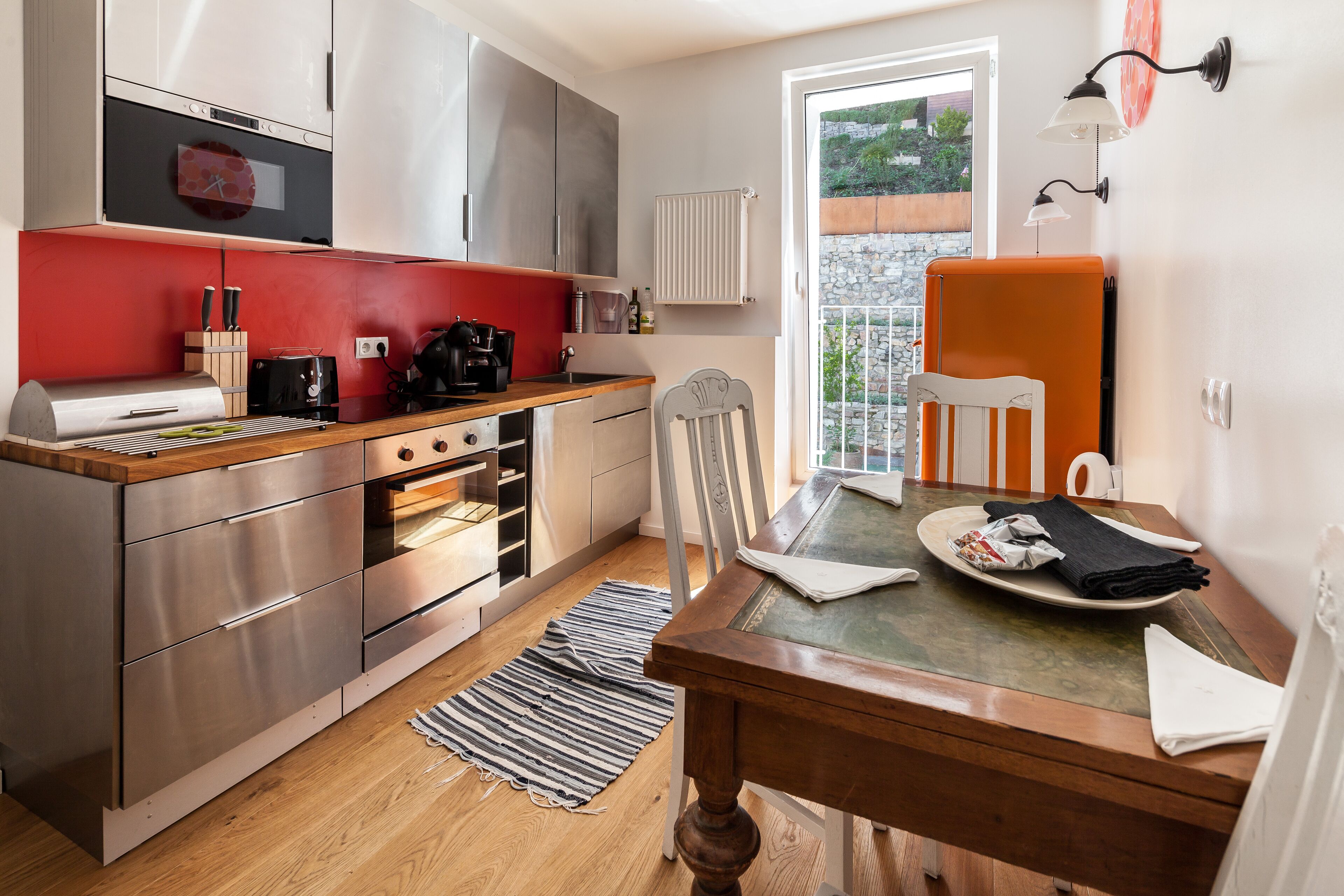 A modern kitchen with stainless steel appliances, a red backsplash, and a dining area with a wooden table and chairs.