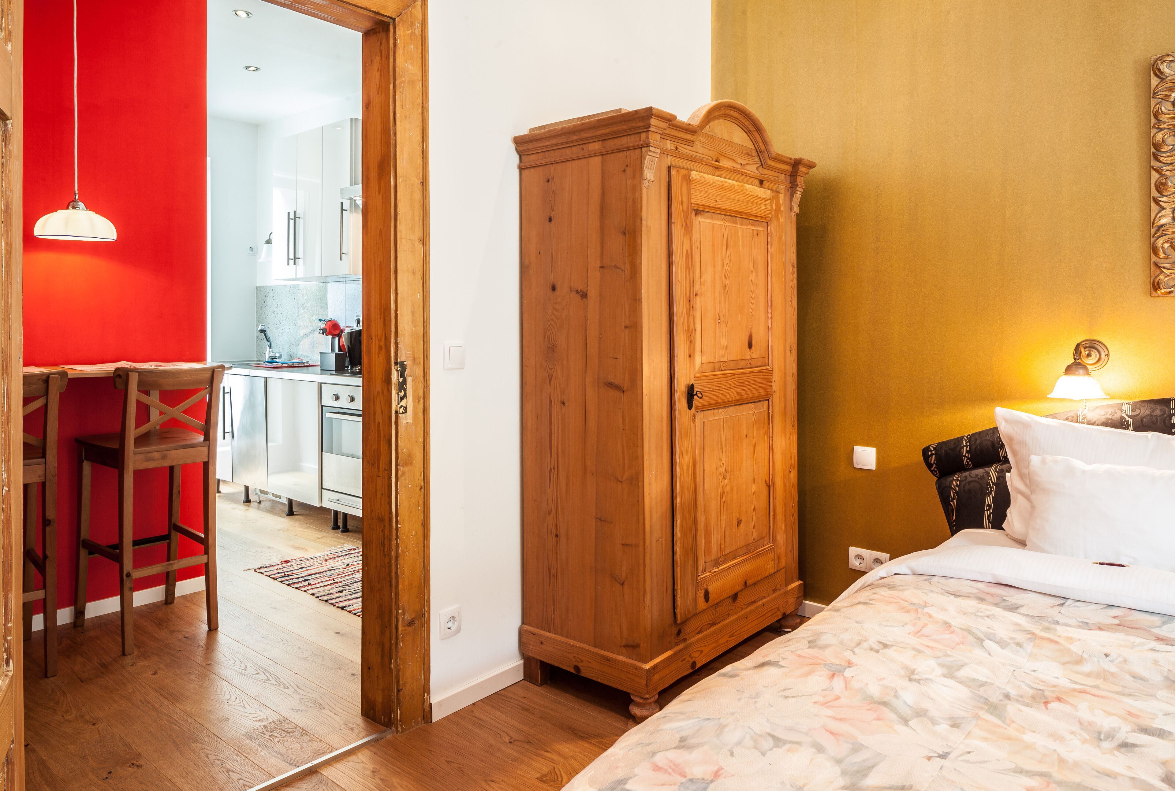 Een slaapkamer met een houten garderobe, een bed met een bloemenprint en een rode muur.