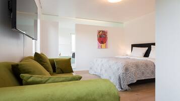 A room with a bed, a green sofa, a painting on the wall, and a flat-screen TV mounted on the wall.