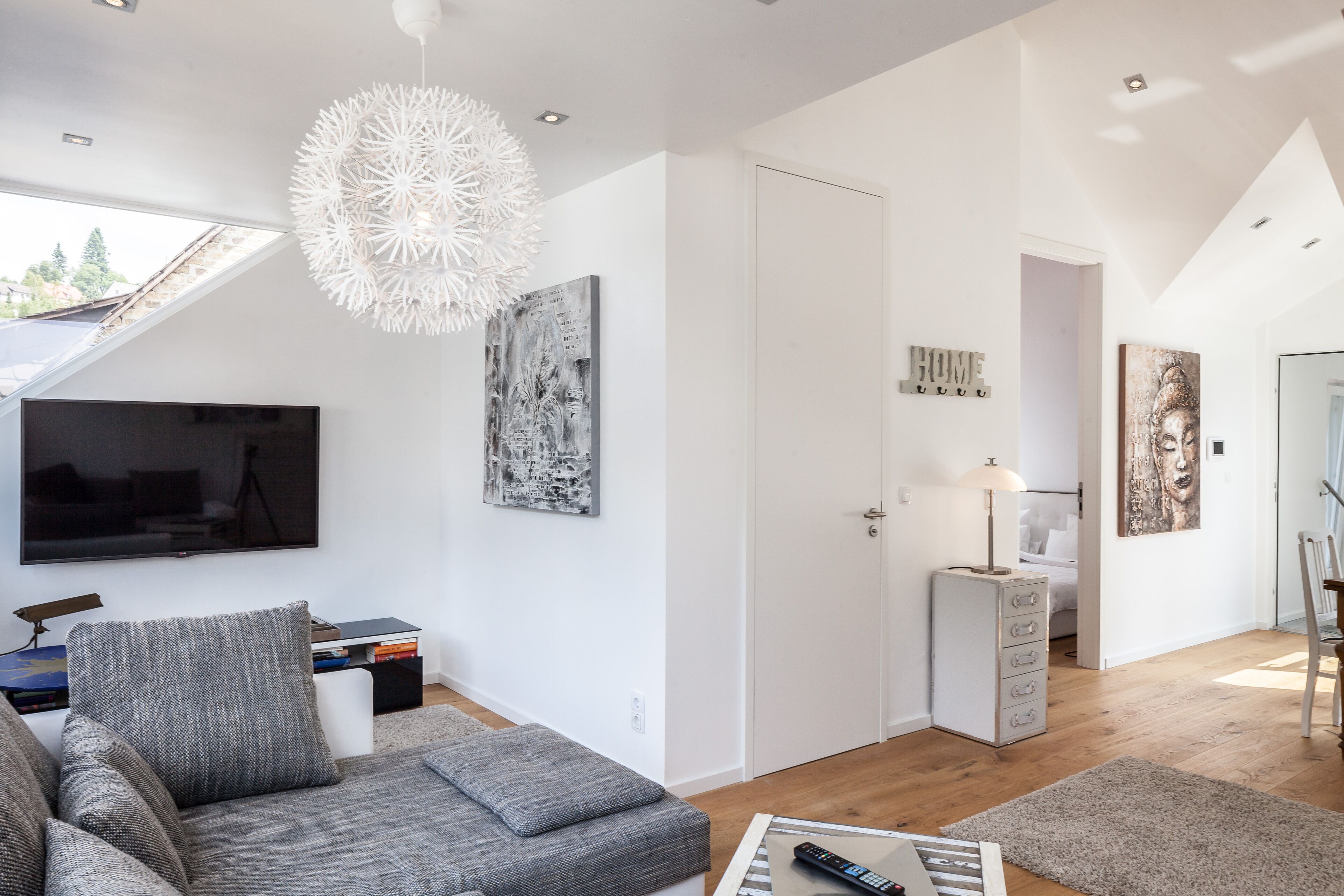 A modern living room with a grey sofa, a flat-screen TV, and a unique ceiling light fixture.