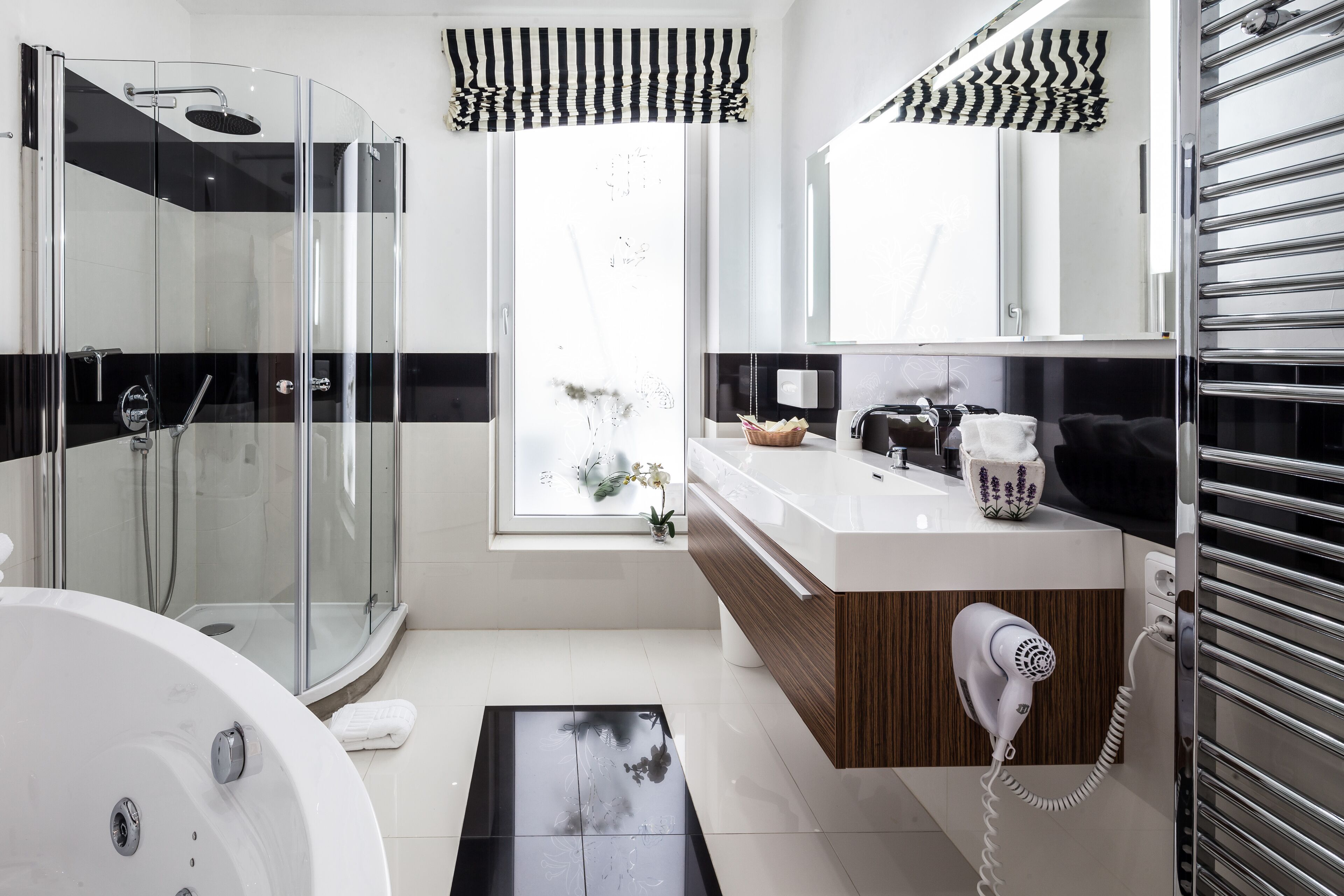 A modern bathroom with a glass-enclosed shower, a white bathtub, a vanity with a mirror, and a hairdryer on the counter.