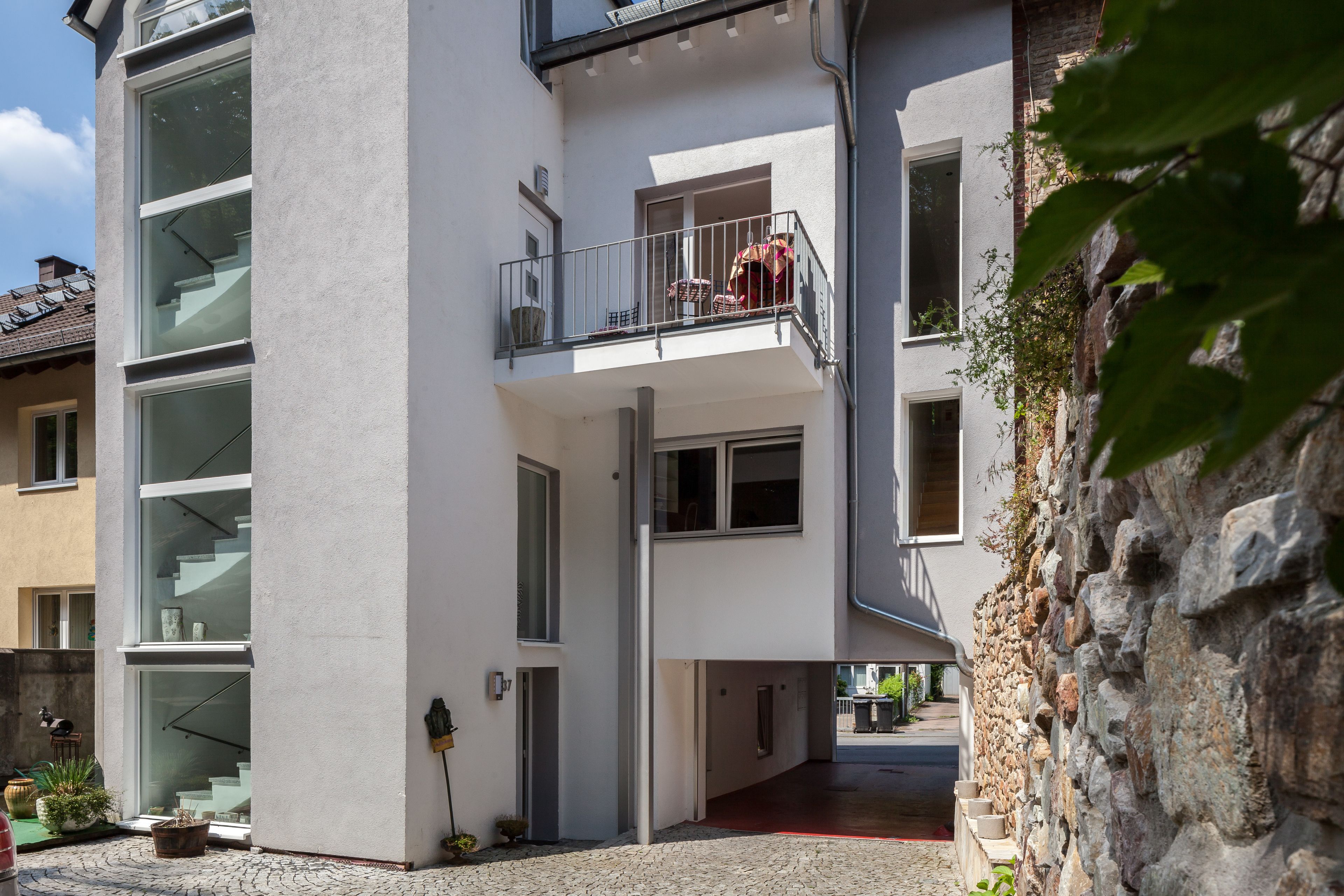 Um edifício moderno de vários andares com varanda, janelas amplas e uma parede de pedra.