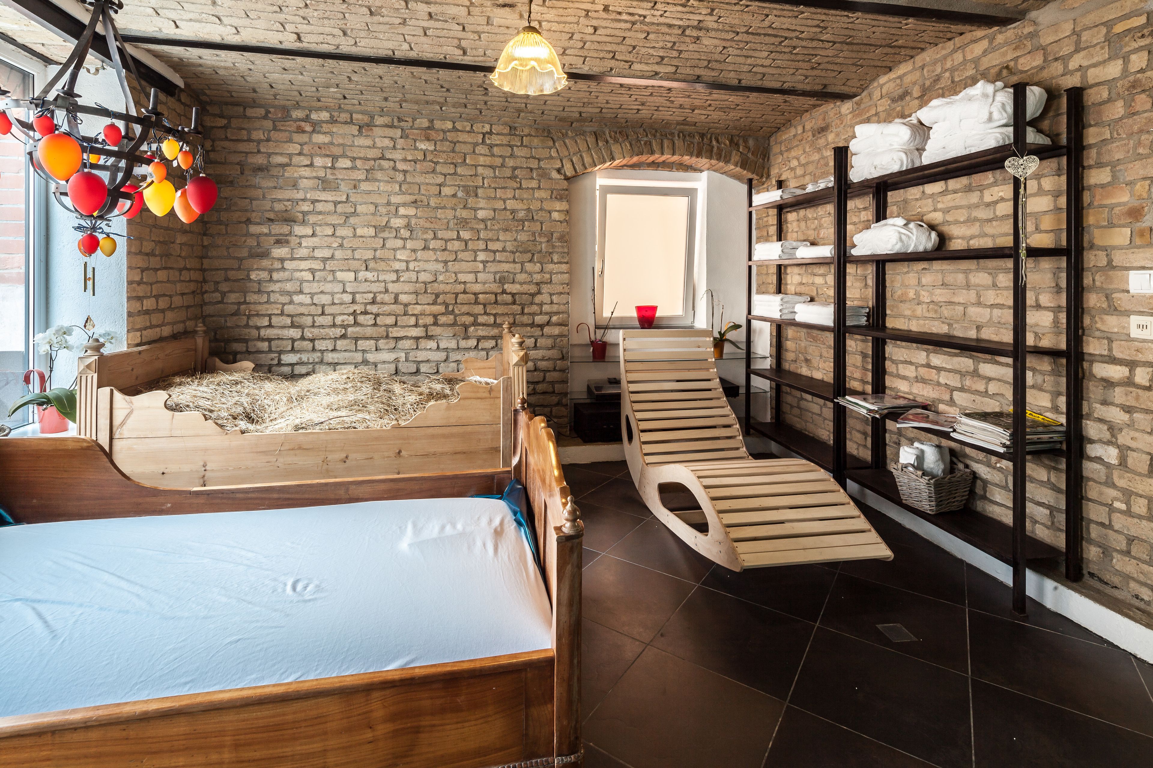 A room with a wooden bed, a bench, a shelf with towels, and a brick wall.