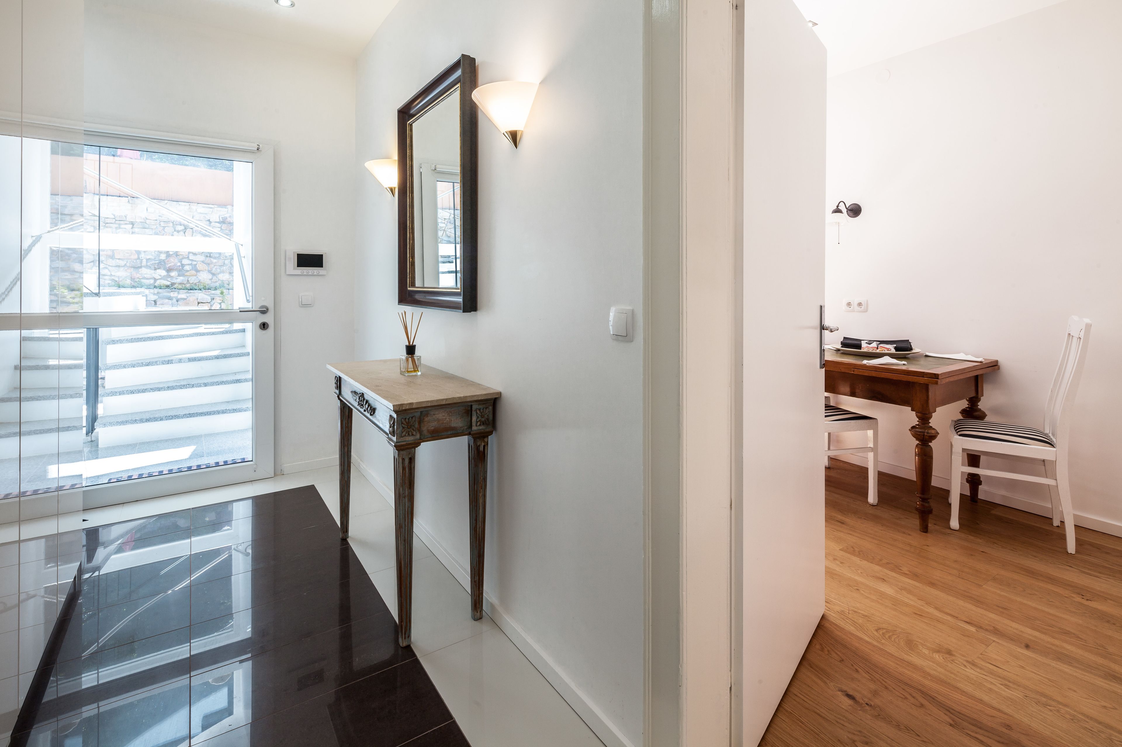 A hallway with a wooden table and chairs, a mirror, and a door leading to a balcony.