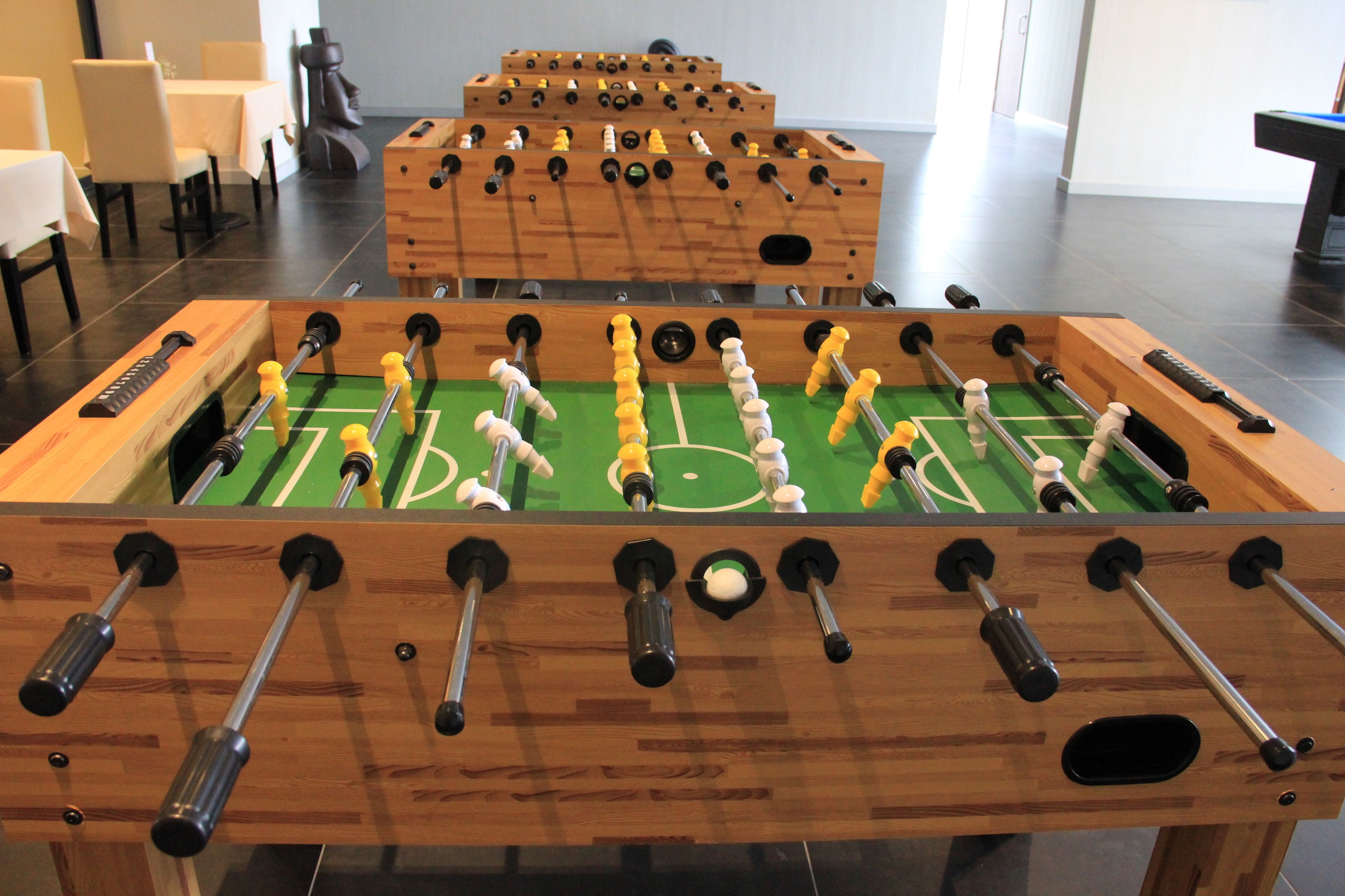 A foosball table in a room with a dining area and a pool table in the background.