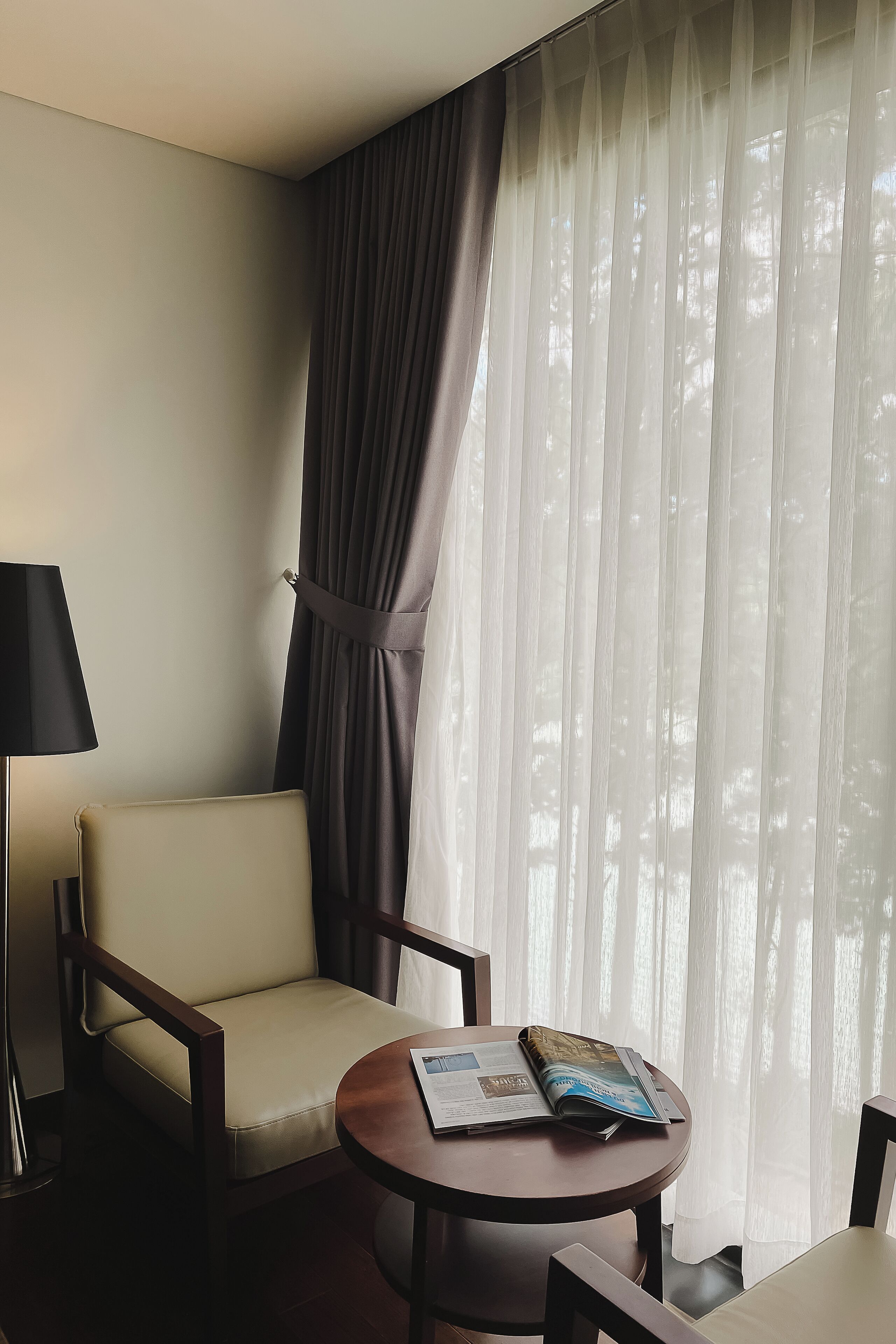A hotel room with a chair, a table, and a lamp.