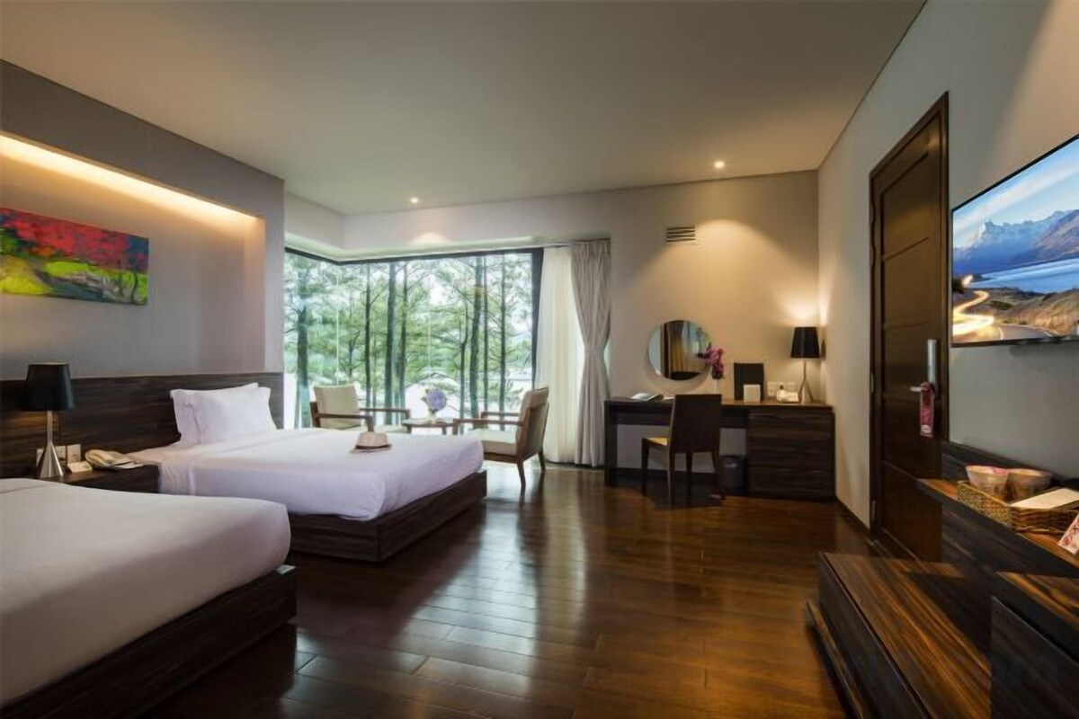 Habitación de hotel con dos camas, un escritorio, una silla, un televisor y un ventanal grande.