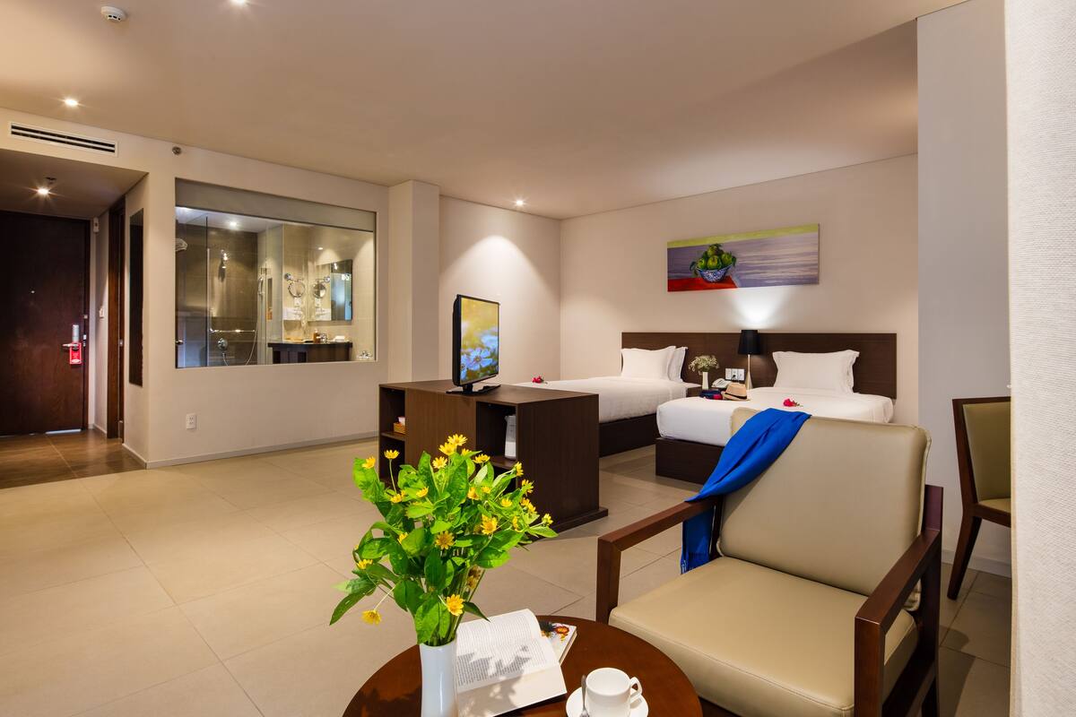 Ein Hotelzimmer mit einem Bett, einem Schreibtisch, einem Stuhl, einem Fernseher und einer Vase mit Blumen.