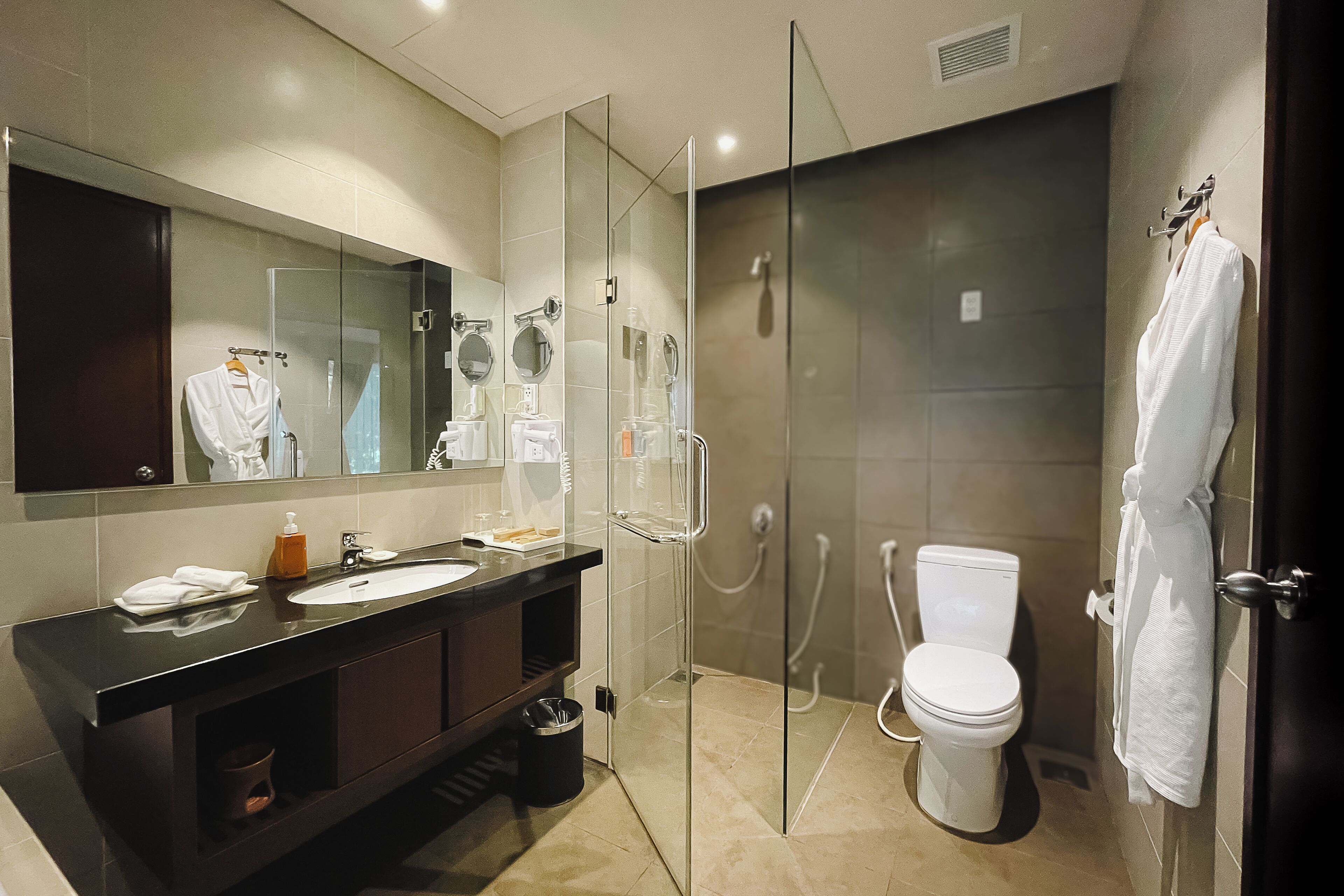 A modern bathroom with a glass-enclosed shower, a white toilet, and a large mirror above a dark wooden vanity.