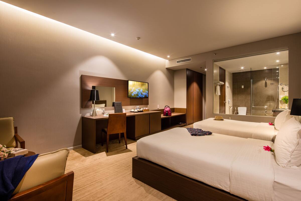 Ein Hotelzimmer mit Schreibtisch, zwei Betten, einer Dusche und einem Fernseher.