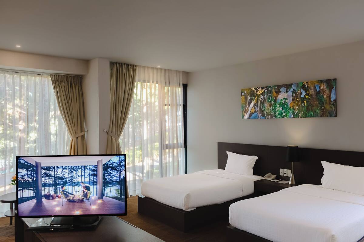 Ein Hotelzimmer mit zwei Betten, einem Fernseher, einem Gemälde und einem Fenster mit Vorhängen.