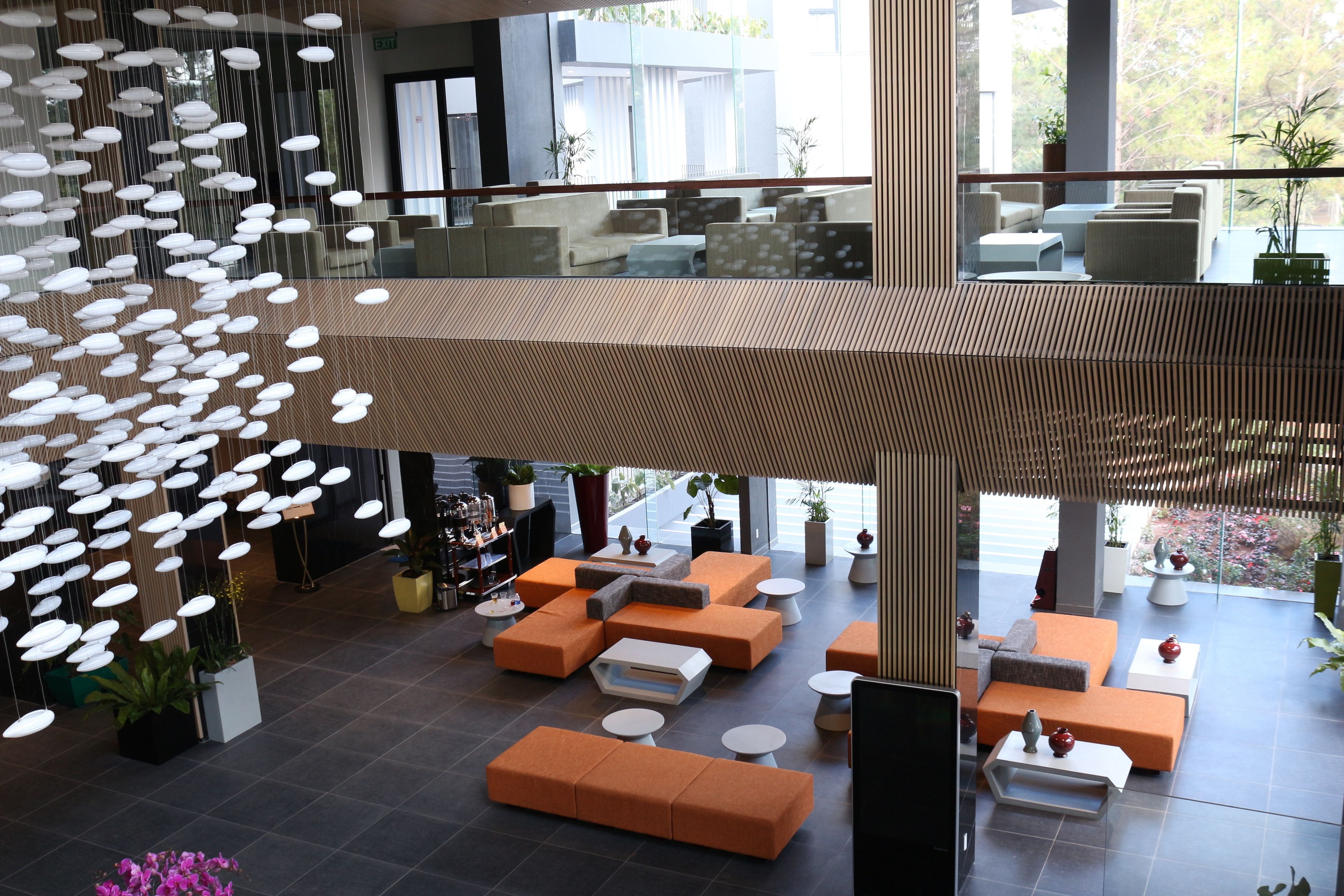 A spacious lobby with multiple seating areas, a suspended light installation, and large windows offering views of the outdoors.