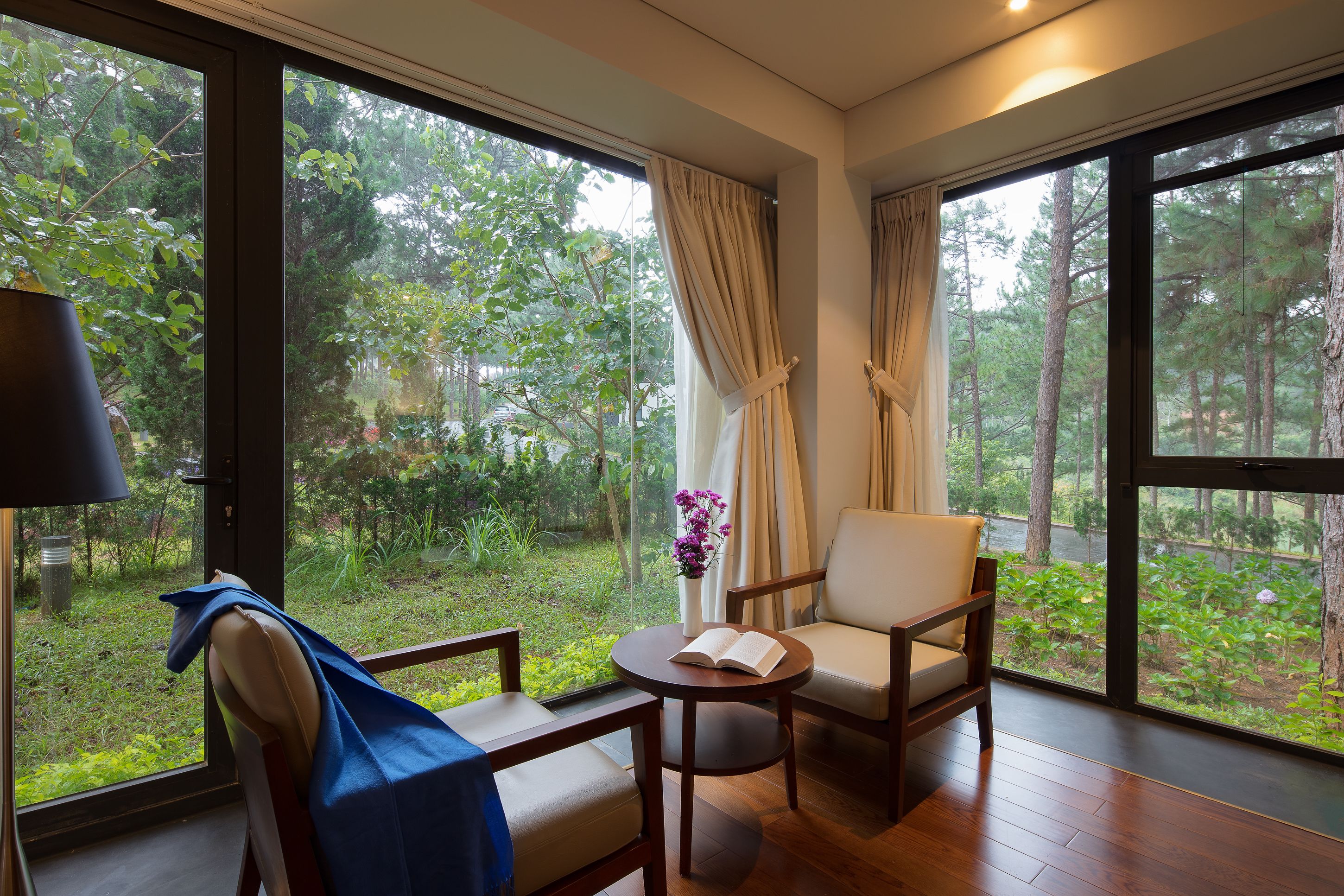 A room with a large window, a chair, a small table, and a lamp.