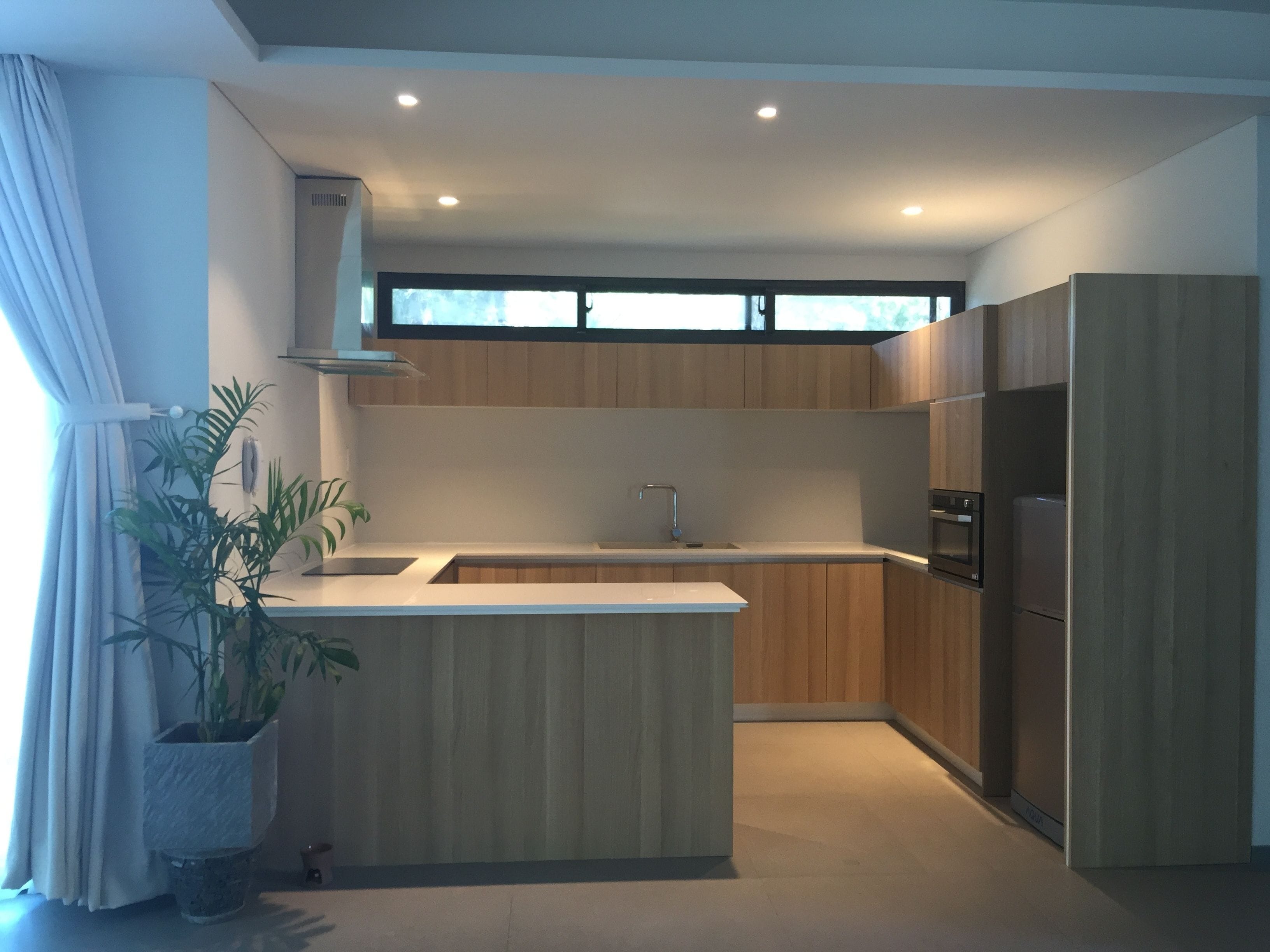 A modern kitchen with wooden cabinets, a central island, a built-in oven, and a window above the sink.