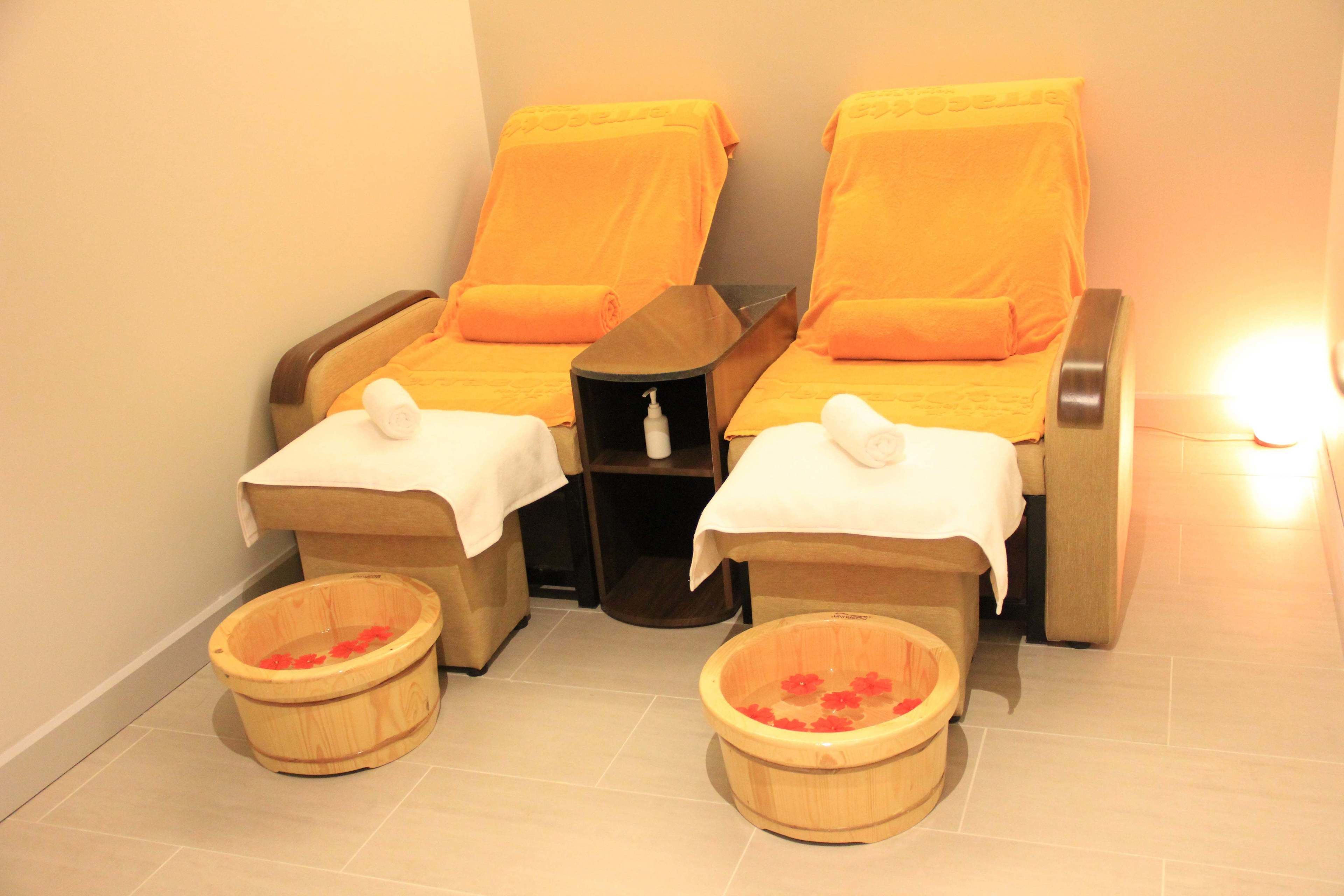 A spa room with two massage chairs, a small shelf with a bottle, and two wooden basins with red flowers.