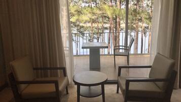 A room with two chairs and a small table, a view of trees and a railing through a window.