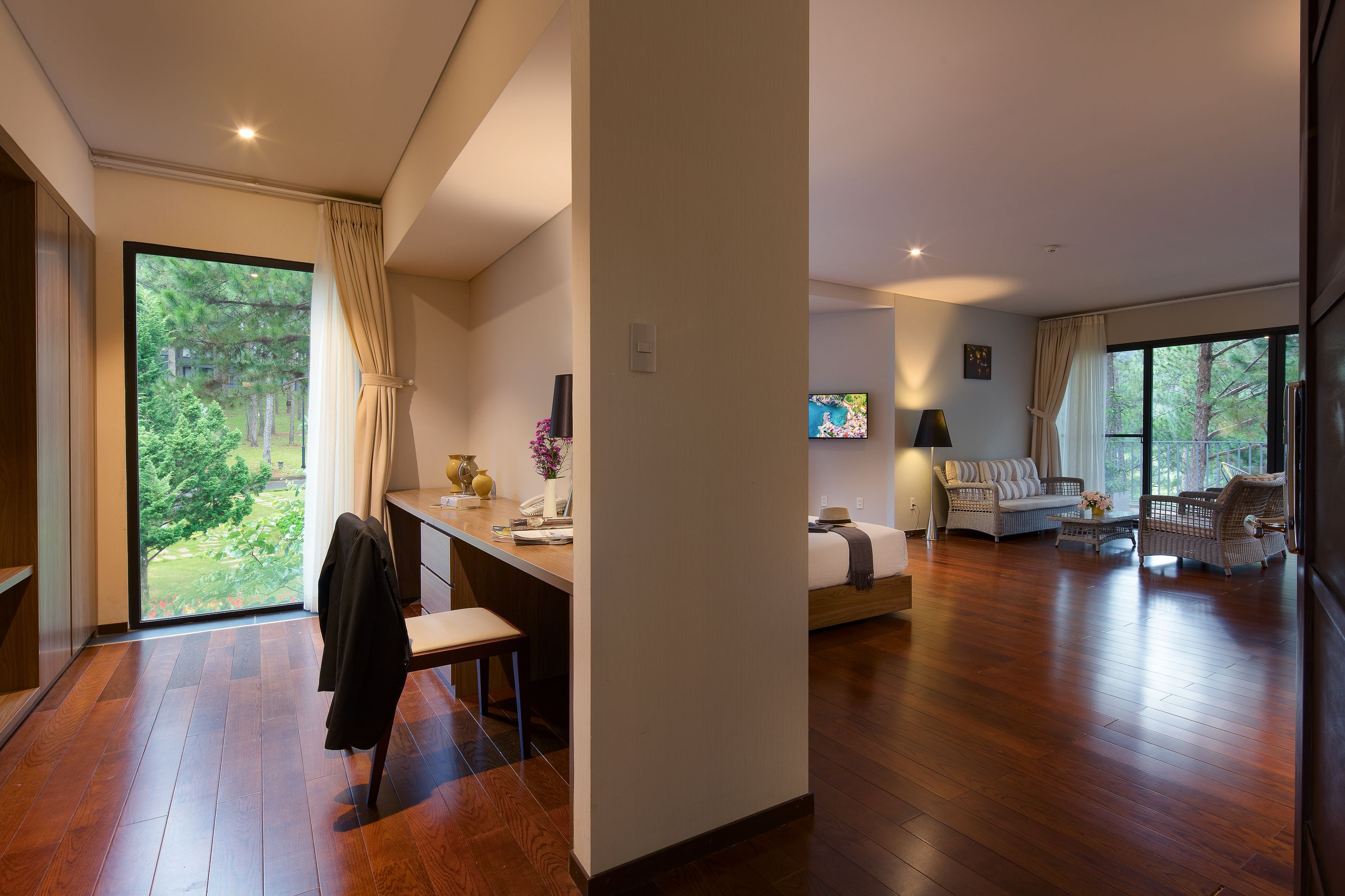 Una habitación amplia con piso de madera, un escritorio con silla, un sofá y una televisión.