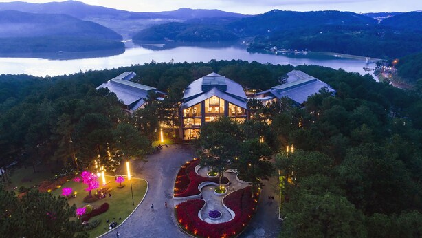 A large, modern hotel with a central dome structure, surrounded by landscaped gardens and a view of a lake and mountains. - Terracotta Hotel & Resort Dalat (Xuan Huong - Da Lat)