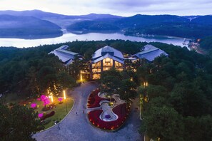 A large, modern hotel with a central dome structure, surrounded by landscaped gardens and a view of a lake and mountains. - Terracotta Hotel & Resort Dalat (Xuan Huong - Da Lat)