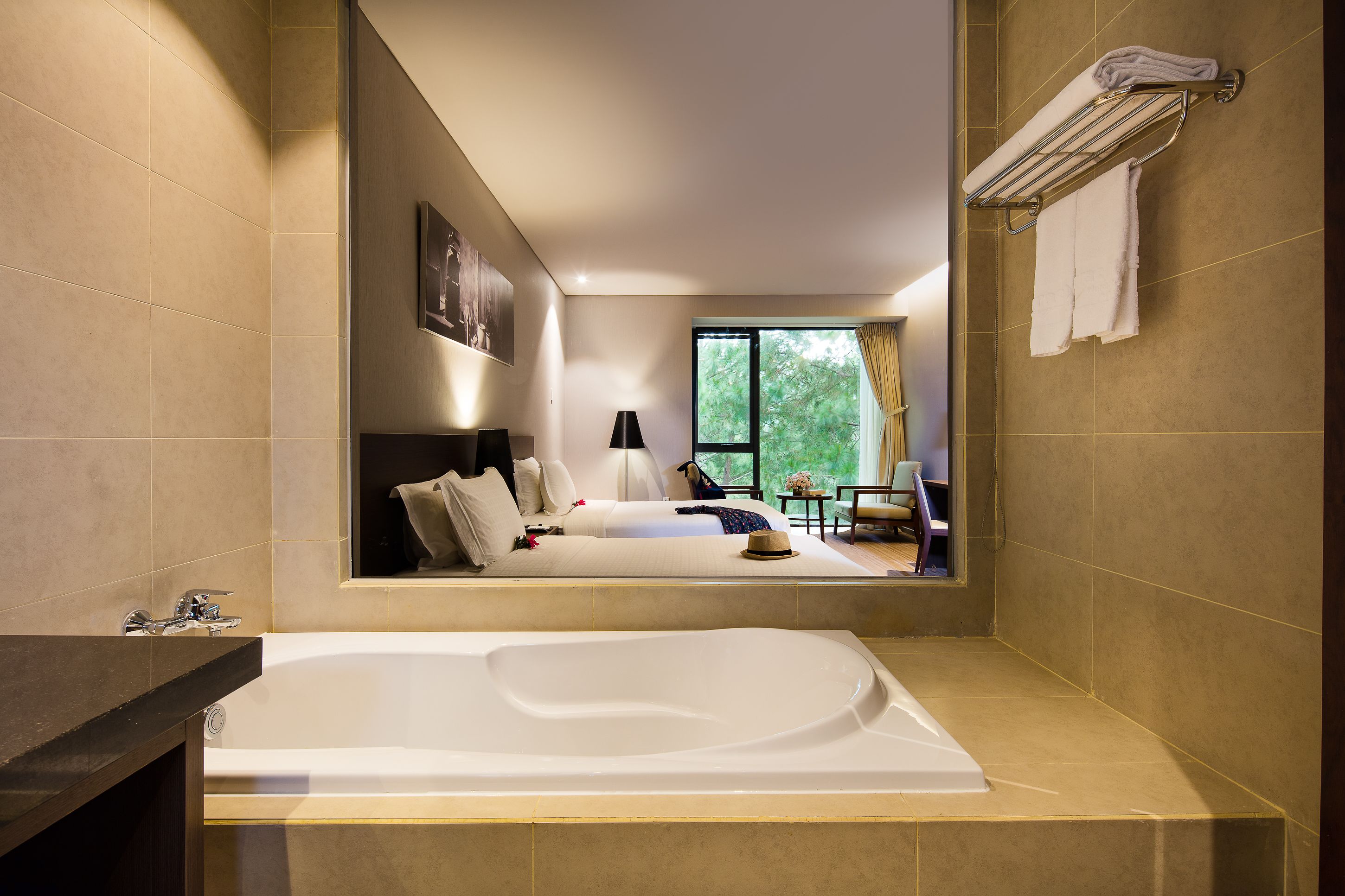 A modern bathroom with a large bathtub, a sofa bed, and a view of a bedroom with a window.