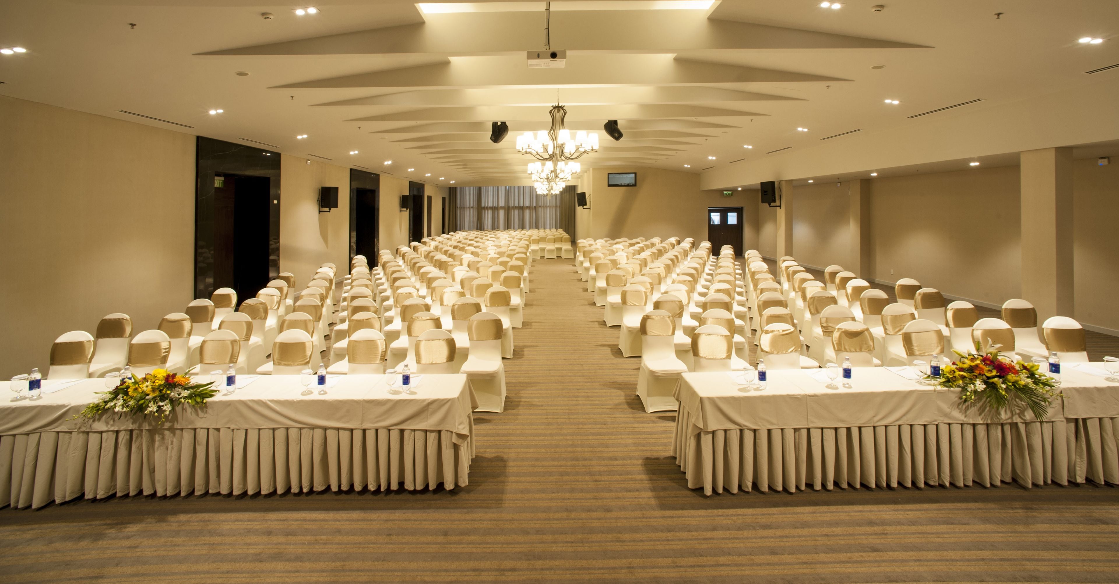 Une salle de conférence avec des rangées de chaises et de tables, un lustre et une scène à l’avant.