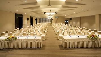 Une salle de conférence avec des rangées de chaises et de tables, un lustre et une scène à l’avant.