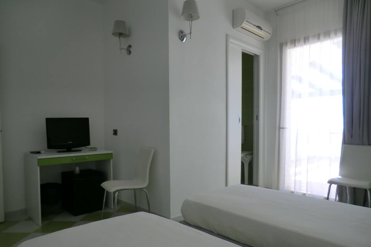 A hotel room with two beds, a desk with a computer, a chair, and an air conditioning unit.