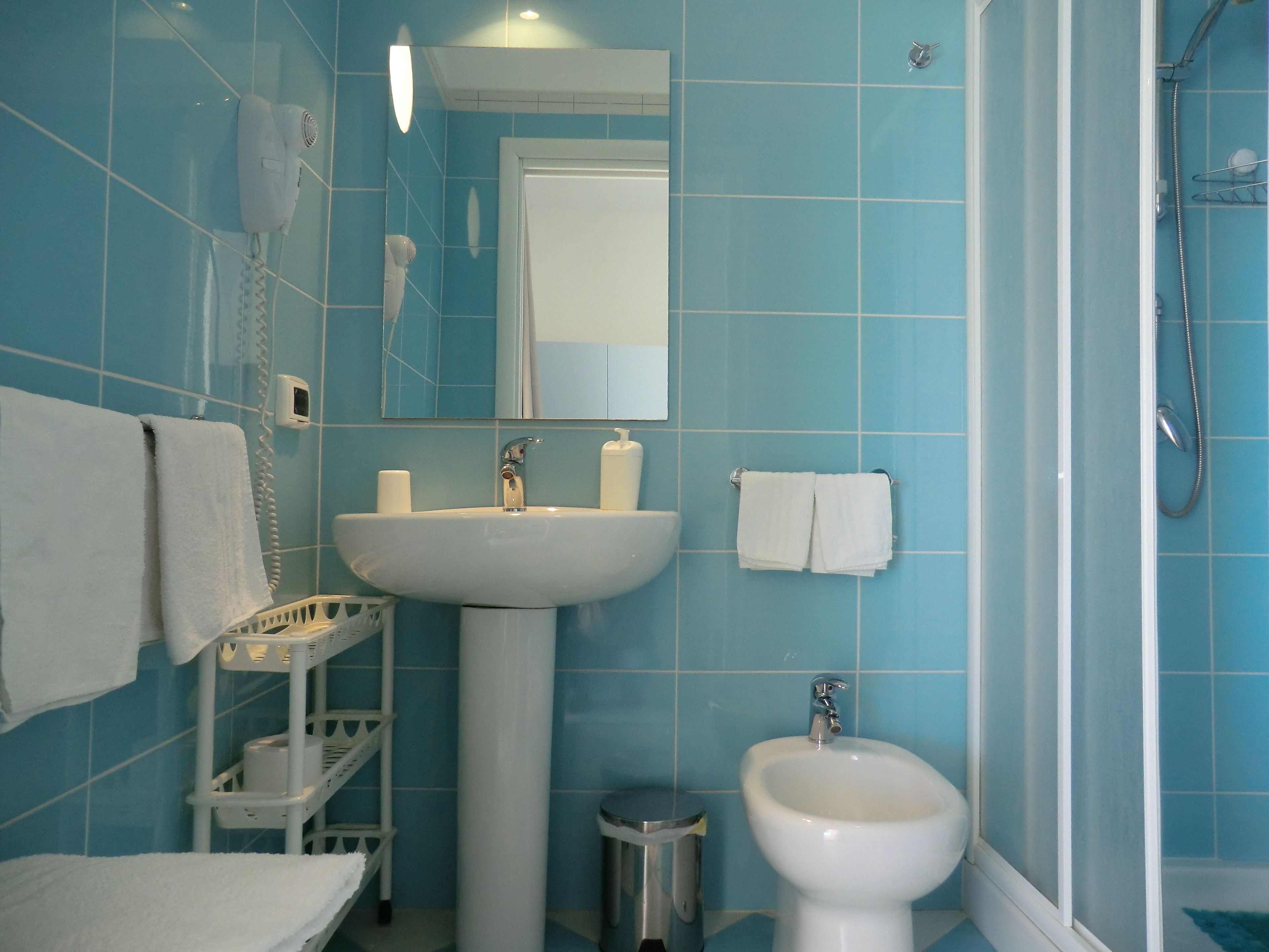 A bathroom with blue tiles, a sink, a bidet, a mirror, and a towel rack.