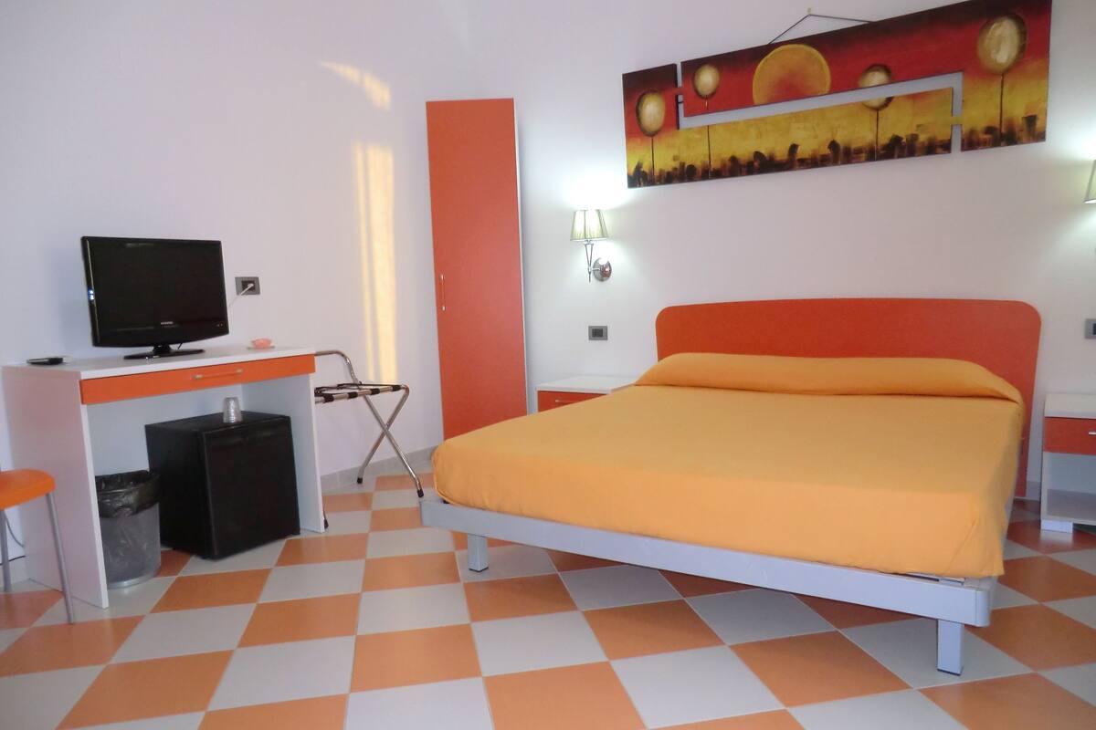 A room with a bed, a desk, a television, and a painting on the wall.