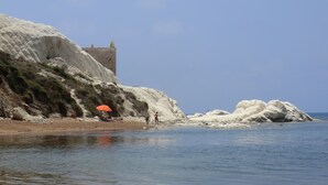 A coastal landscape with white rock formations, a tower, and a beach with people and an umbrella. - B&B Mediterraneo Mare e Sole (Palma di Montechiaro)