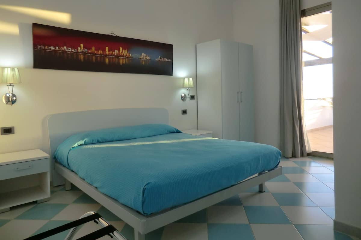 A bedroom with a bed, a wardrobe, a nightstand, and a wall-mounted lamp.