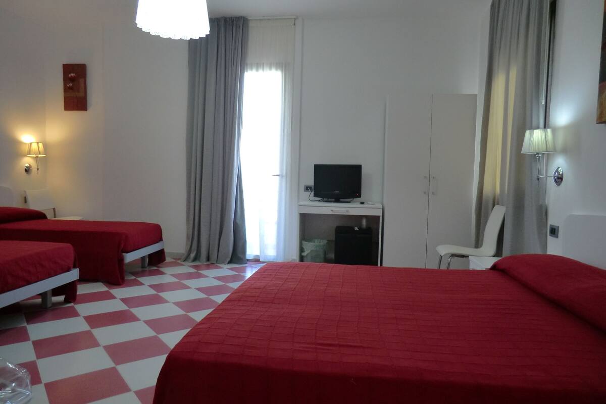 A hotel room with two single beds, a desk with a television, a chair, and a window with curtains.