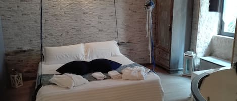 A bedroom with a bed, white linens, a wooden wardrobe, and a window.