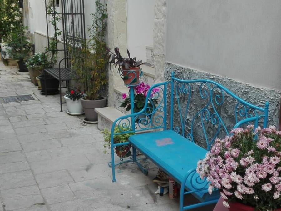 Ein schmaler Gang mit einer blauen Metallbank und einem rosa Tisch mit Blumen.