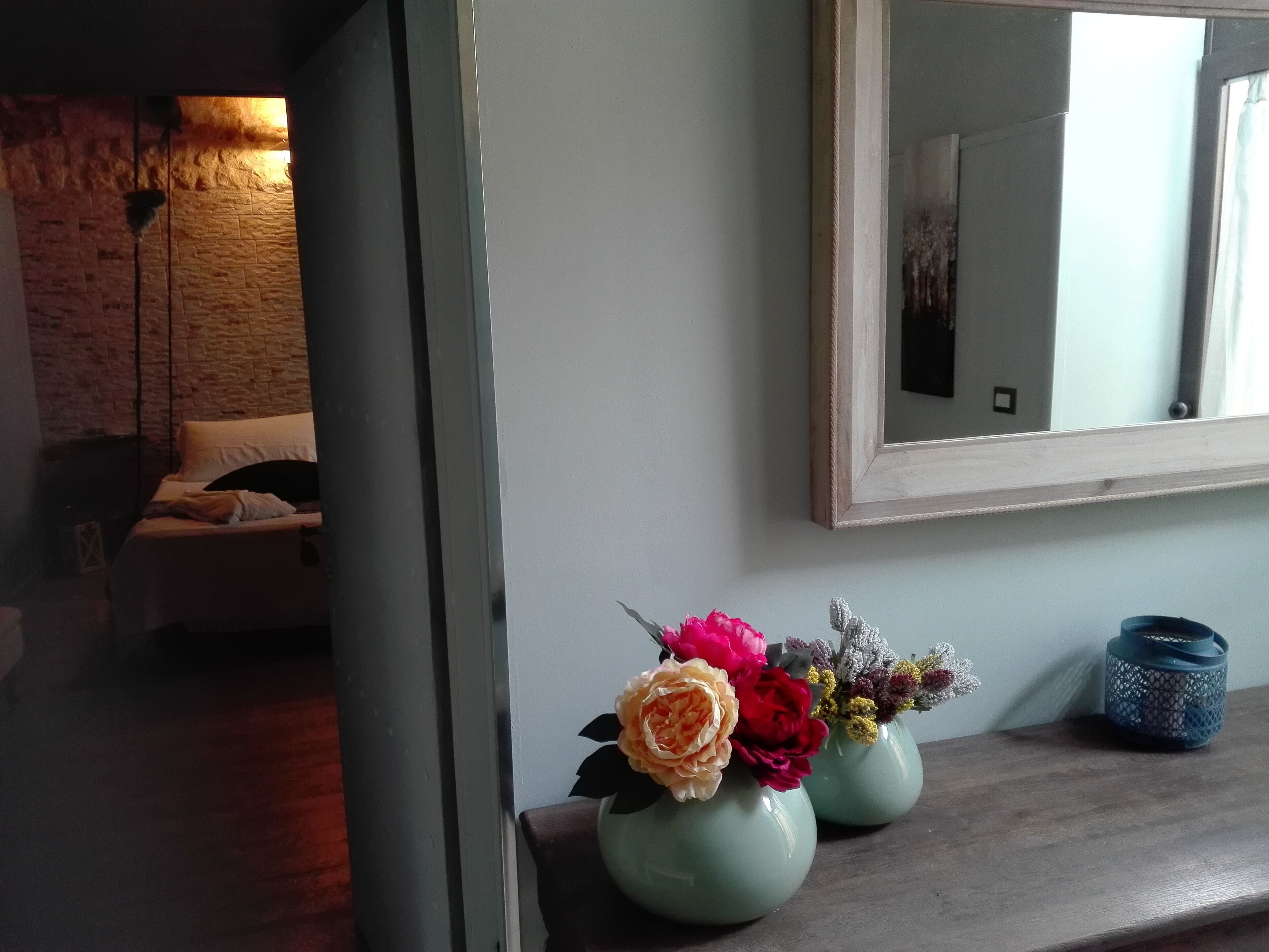 A room with a bed, a mirror, and two flower vases on a wooden shelf.