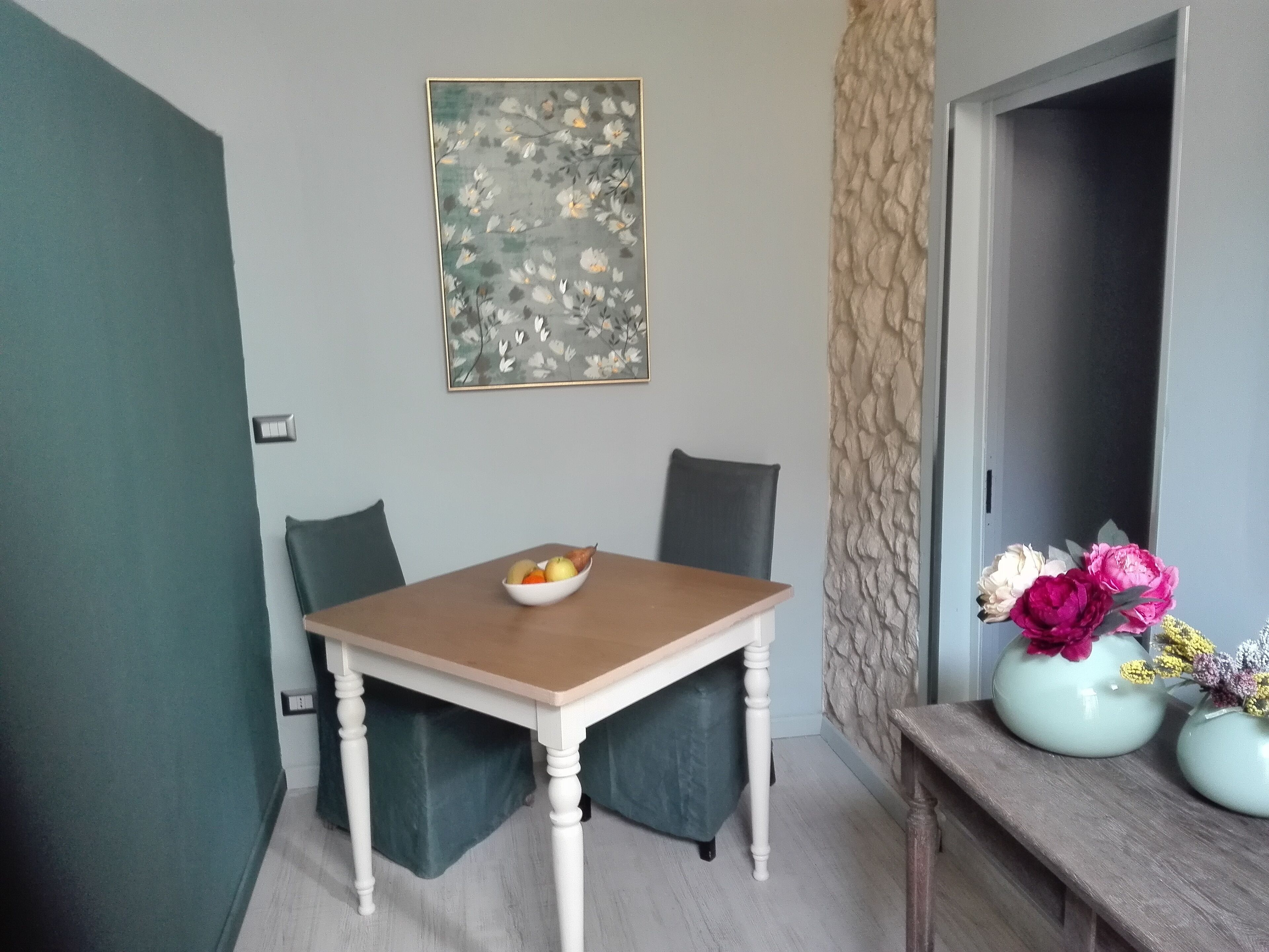A dining table with chairs, a bowl of fruit, and a vase with flowers.