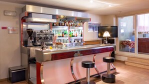 Un espace bar moderne avec un comptoir en acier inoxydable, des tabourets de bar et une variété de bouteilles d’alcool.