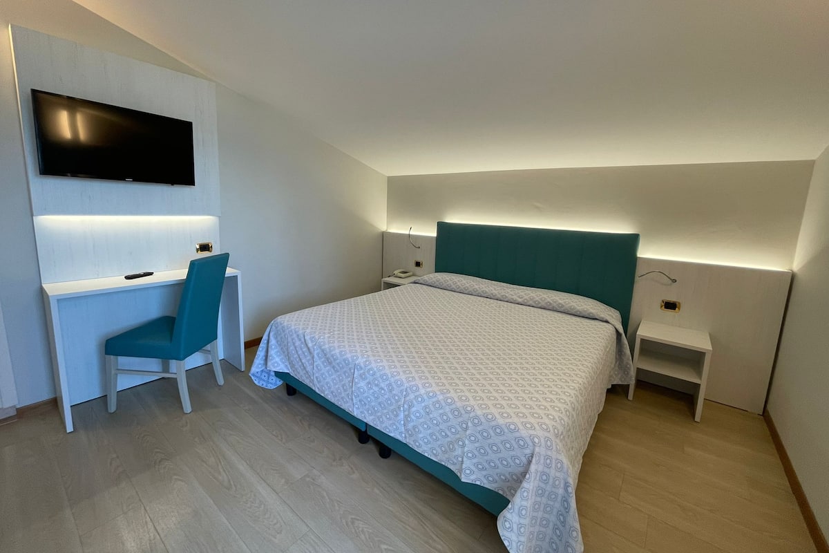 Una habitación de hotel moderna con cama, escritorio, silla, televisión y mesita de noche.