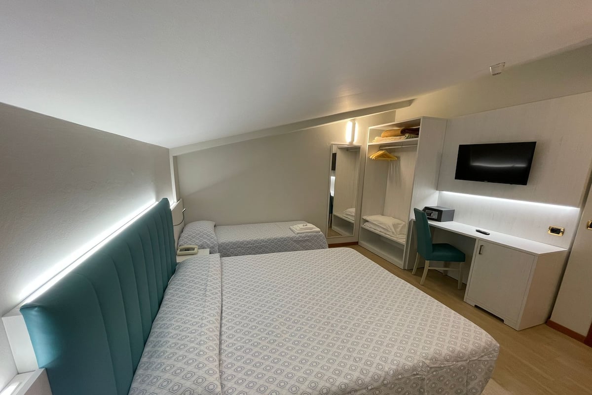 Habitación de hotel con dos camas, un escritorio, una silla, un televisor y un armario.